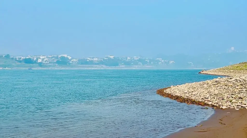 Traveler relaxing on pebble Chongqing beach riverbank at Songji Ancient Town with ferry crossing in distance